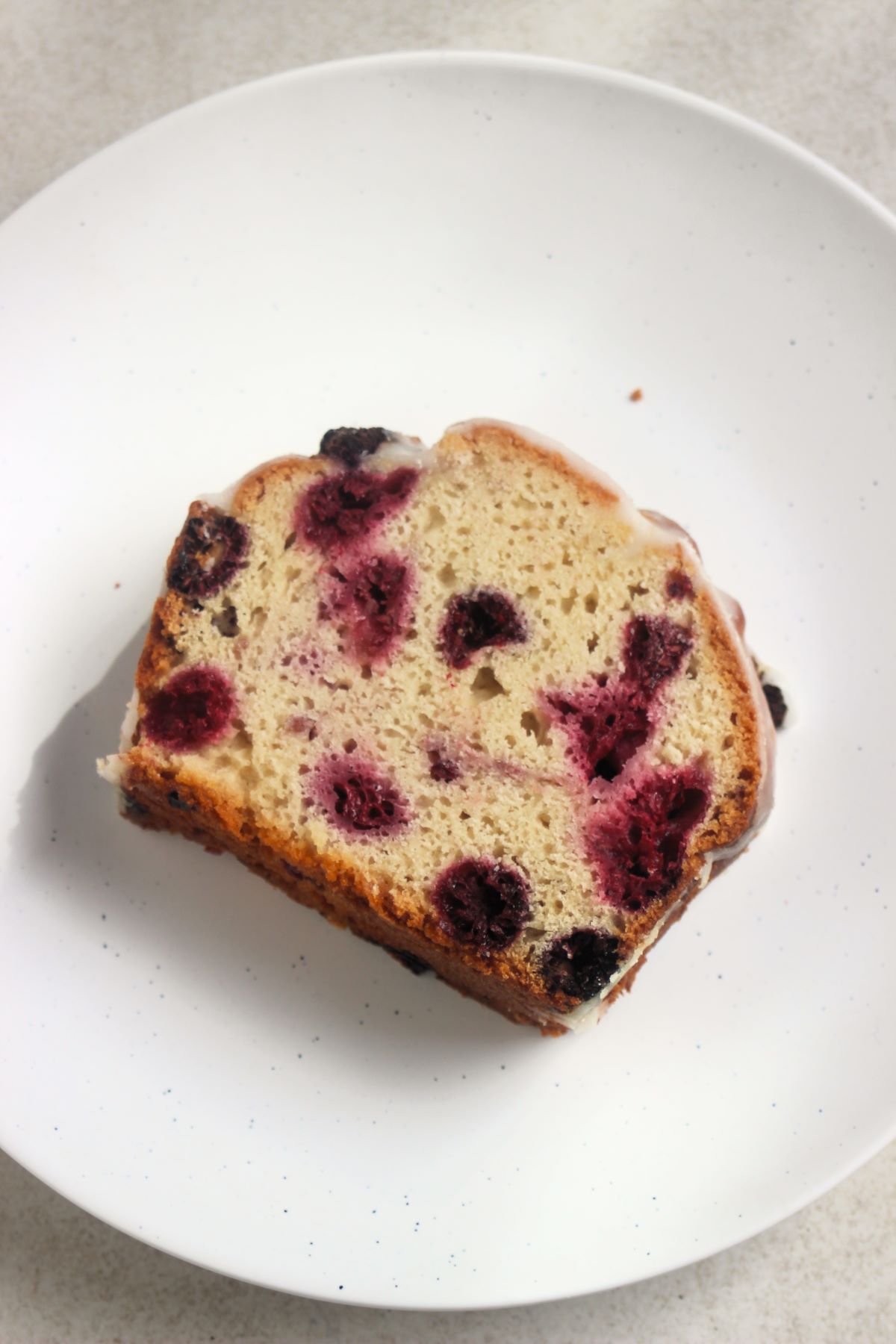 Portion of raspberry loaf cake on a white plate seen from above.