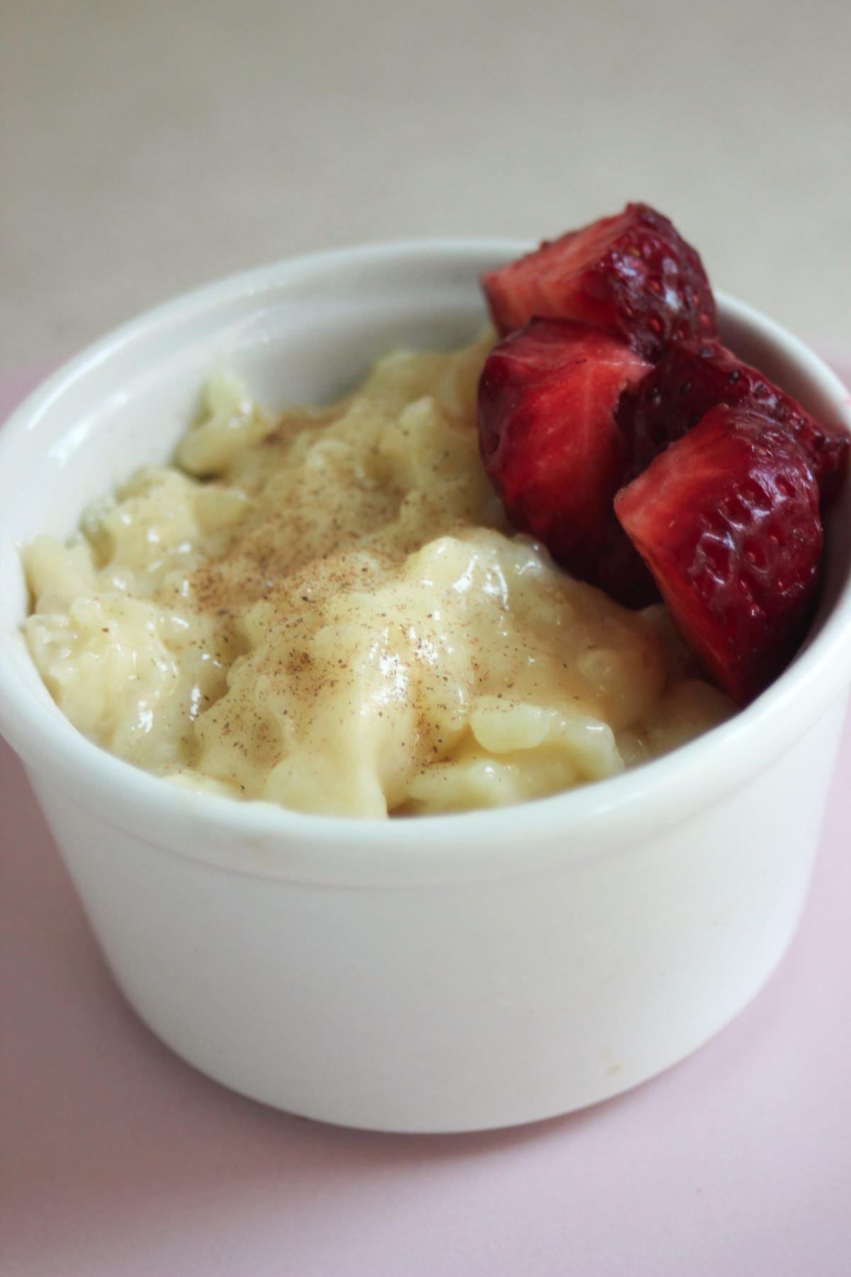 White ramekin with caramel rice pudding and fresh strawberries.