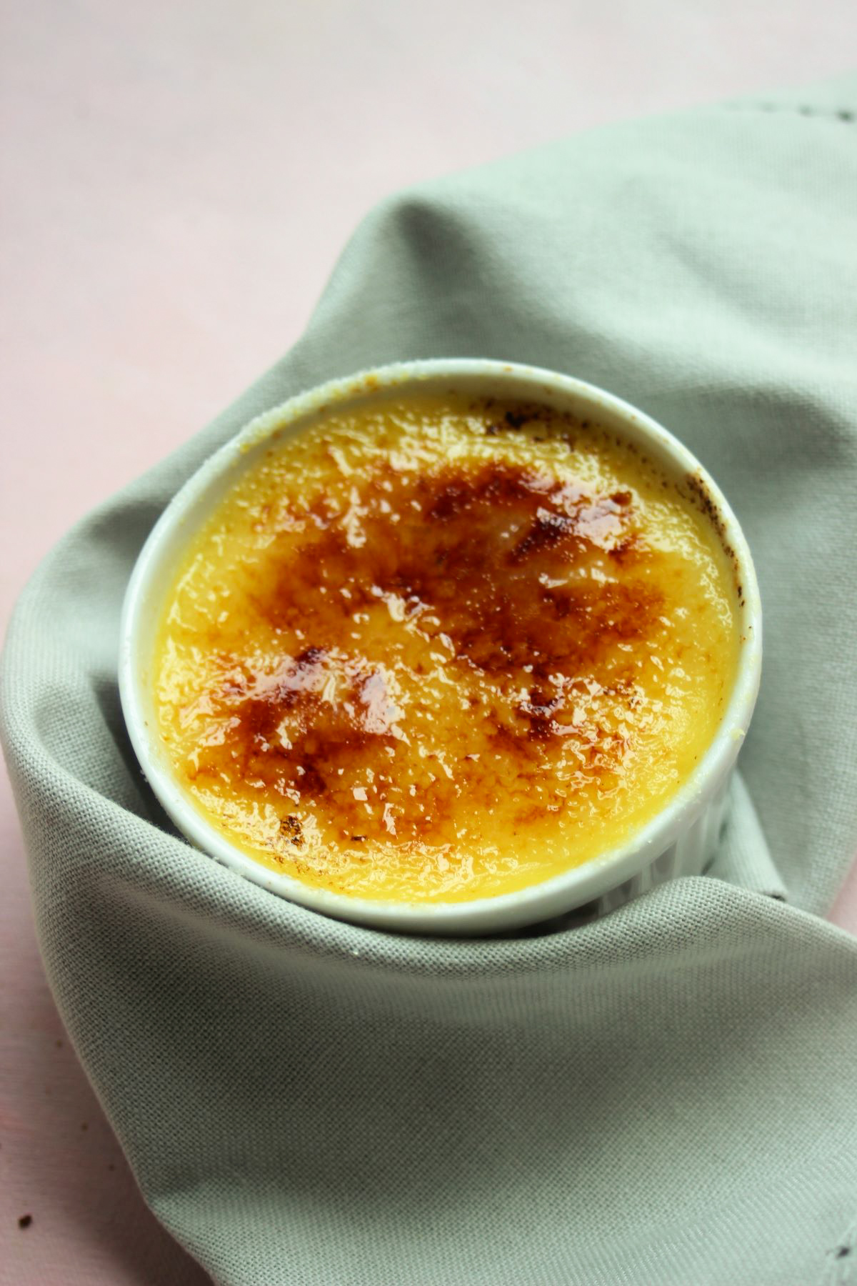 White ramekin with creme brulee wrapped in an aqua-green napkin.