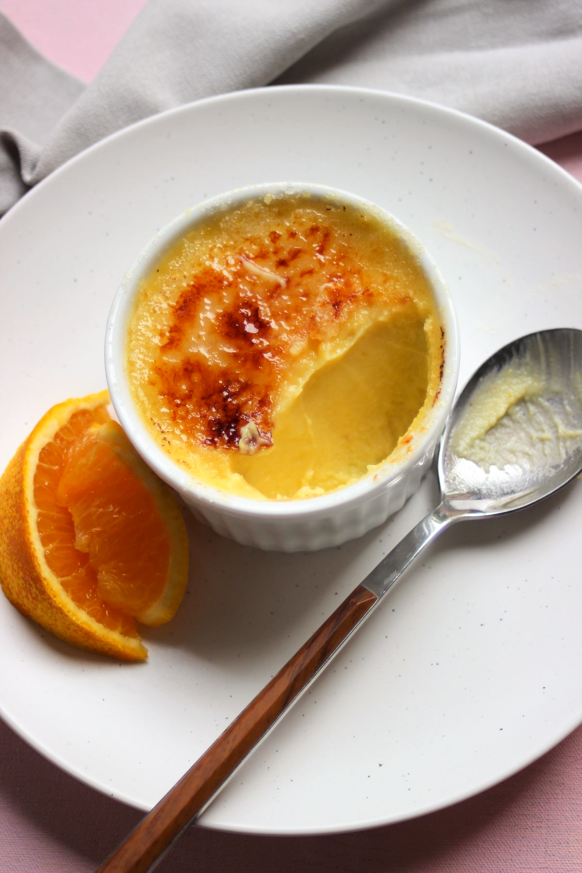 Ramekin with creme brulee without a piece. A spoon with rest of the creme brulee.