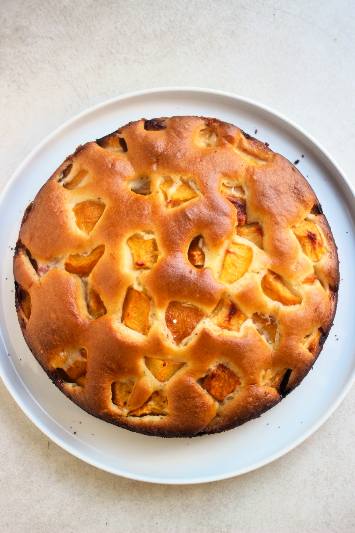 Peach cake on a white plate on a white surface seen from above.