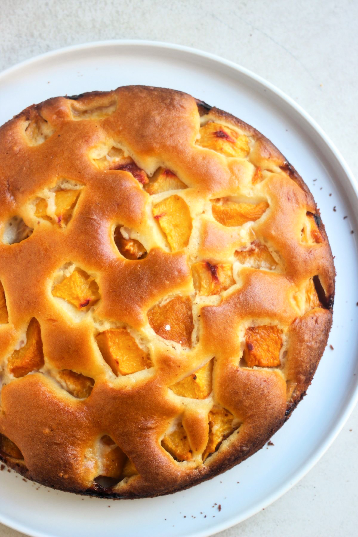 Peach cake on a white plate on a white surface seen from above.