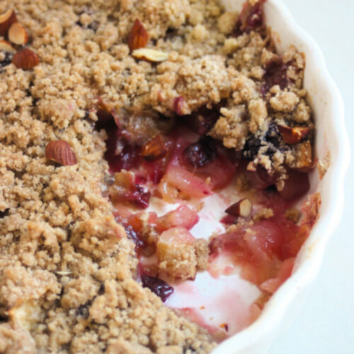 Apple crumble without a piece in a round white baking dish.