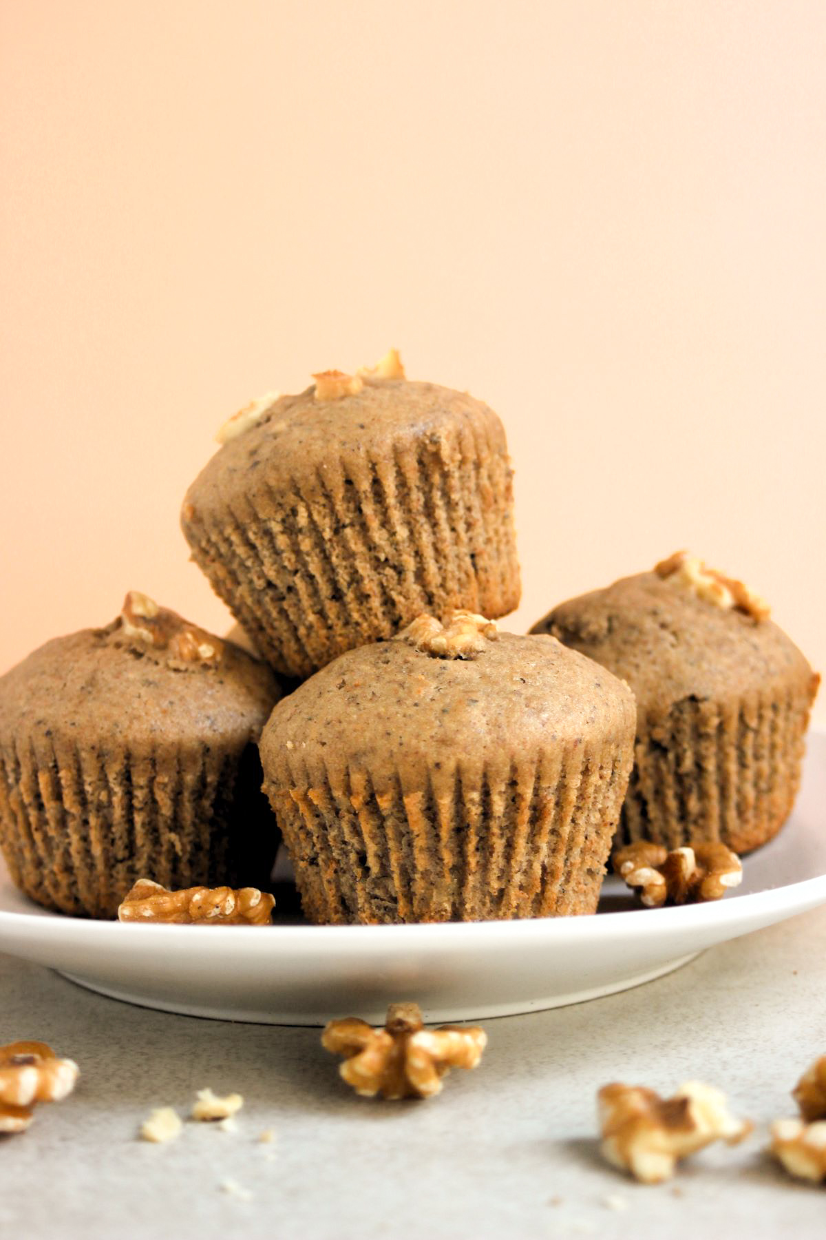 Many banana muffins on a white plate and walnuts scattered around.