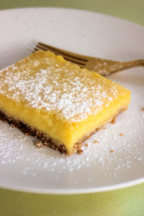 Lemon bar sprinkled with powdered sugar on a white plate.