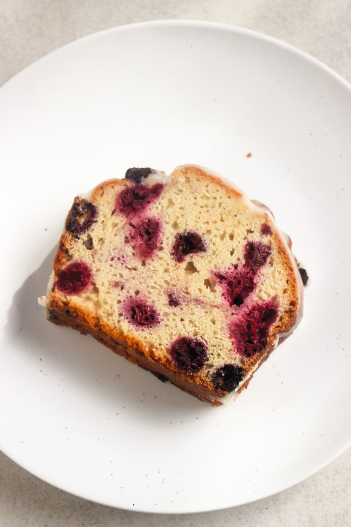 Portion of raspberry loaf cake on a white plate seen from above.