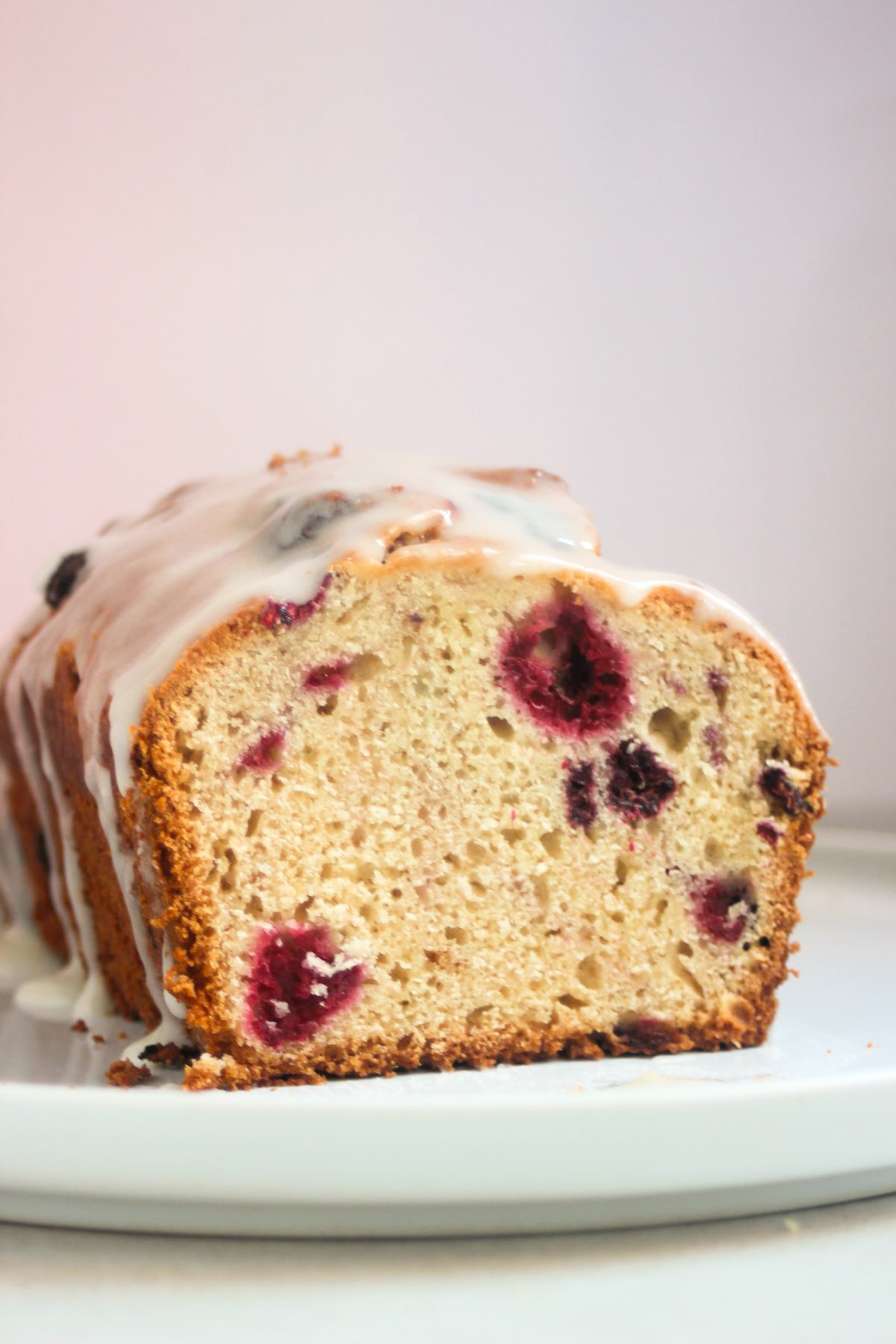 Front view of the inside of raspberry loaf cake with icing on a white plate. Pink background.