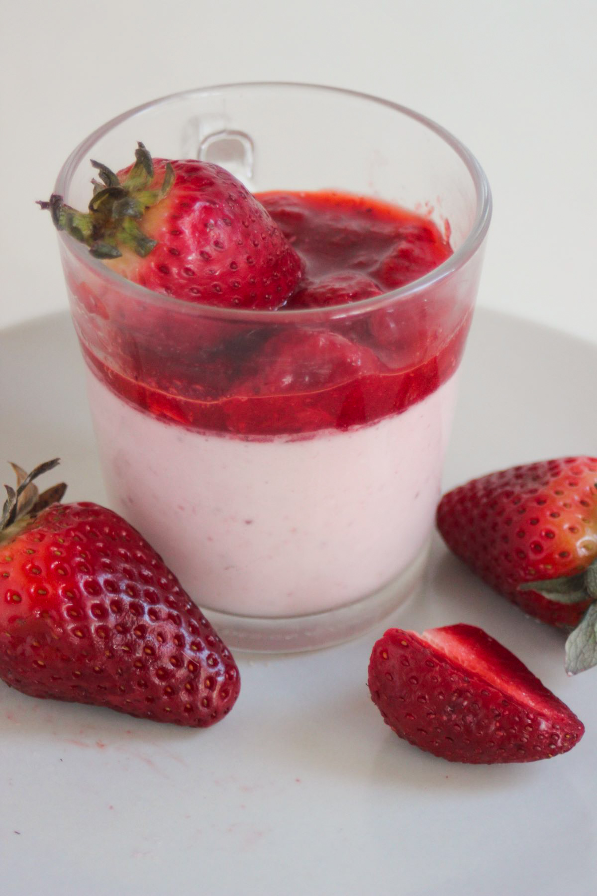 Glass cup with strawberry panna cotta and strawberry sauce. Fresh strawberries on the side.