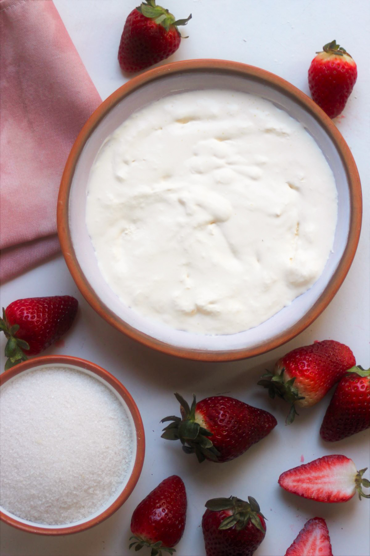 Strawberry Panna Cotta ingredients and a pink napkin on a white surface seen from above.