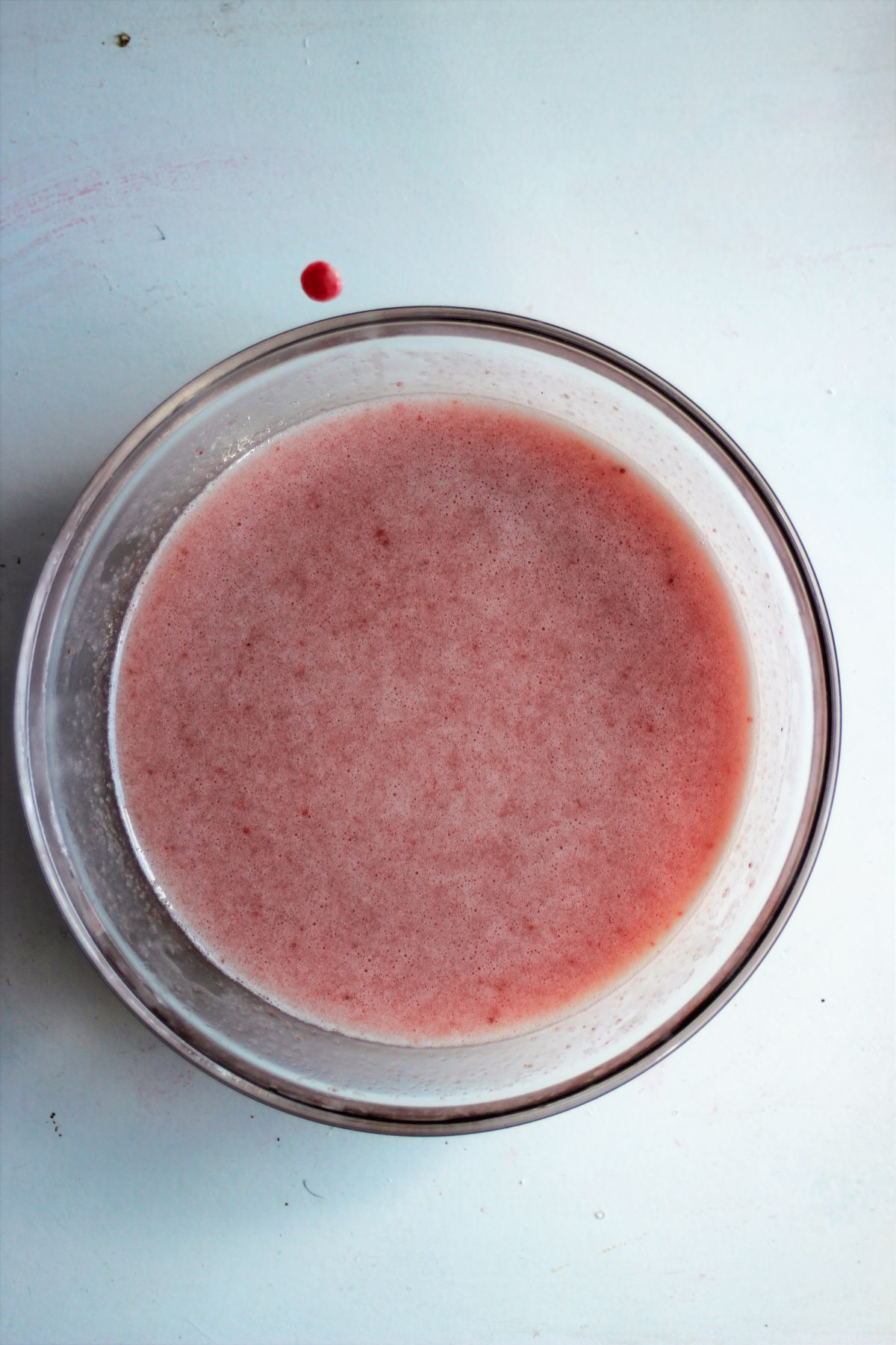 Glass bowl with a pink mixture on a white surface.
