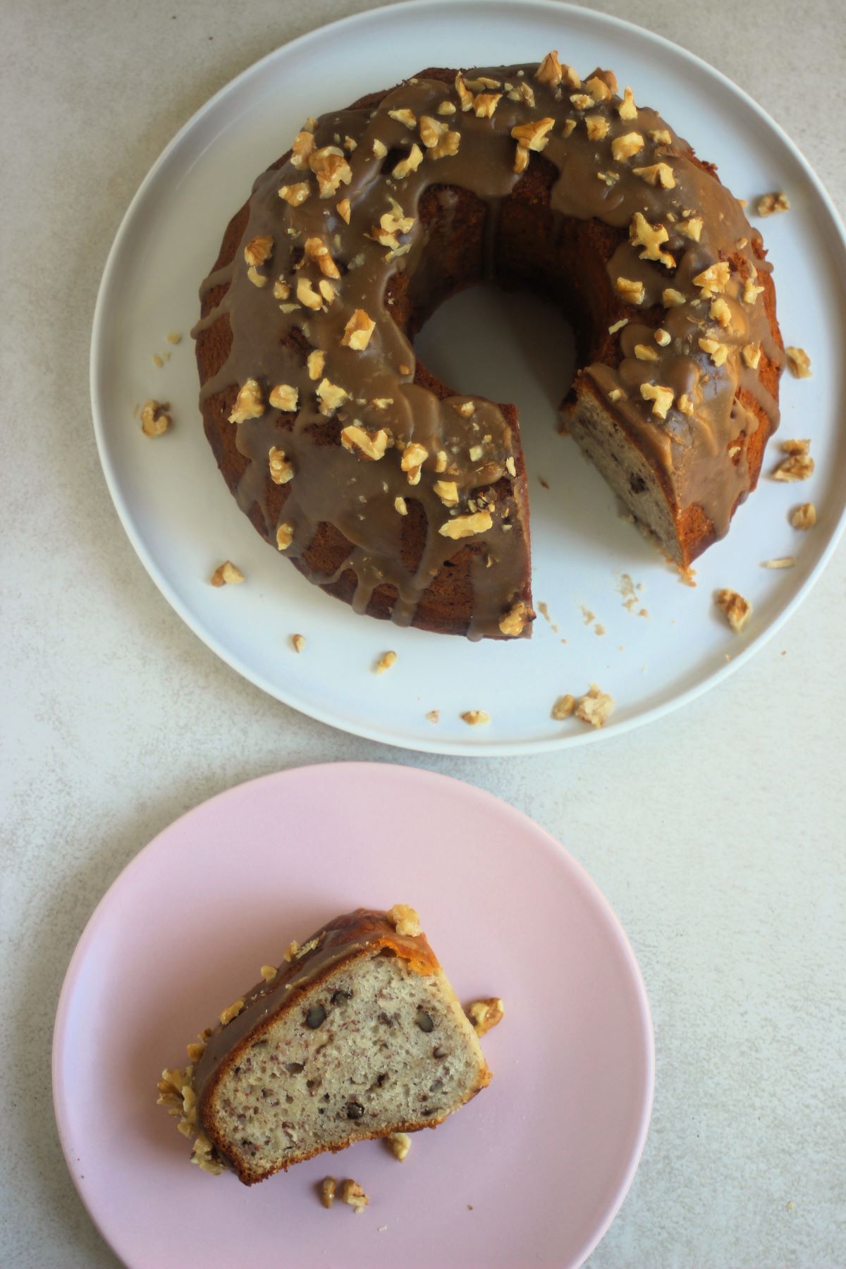 A Portion of banana bundt cake on a pink plate and banana bundt cake on a white plate seen from above.