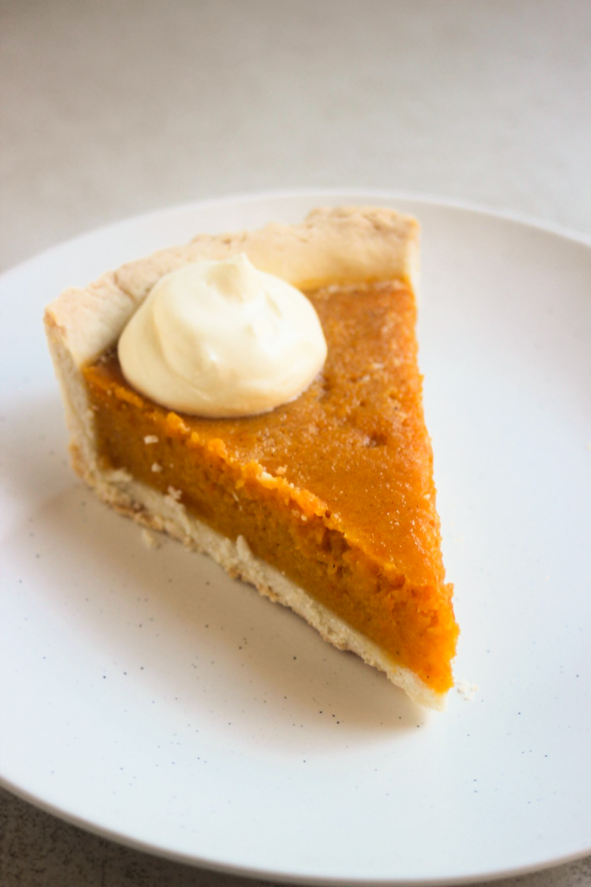 Portion of pumpkin pie en a scoop of whipped cream on a white plate.