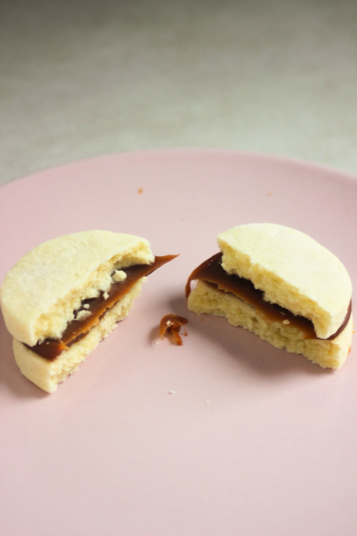 Almond alfajor cut in two pieces on a pink plate.