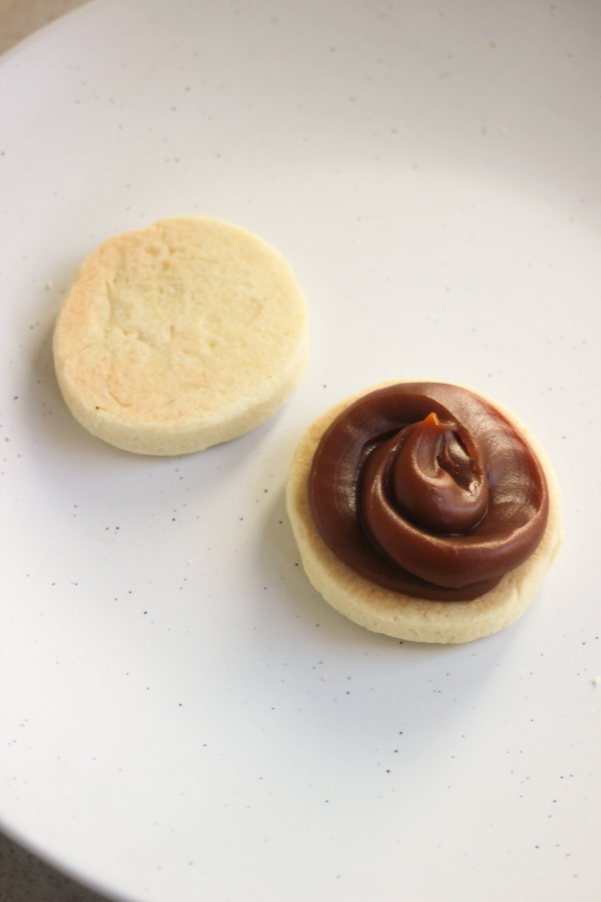 Two biscuits, one with dulce de leche, on a white plate.