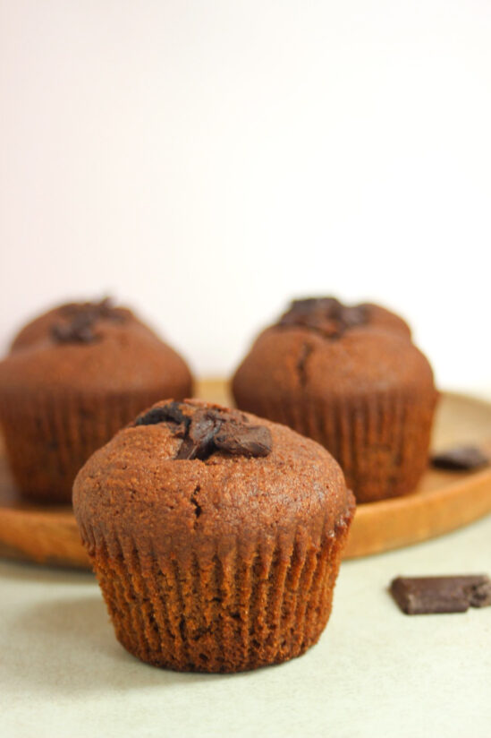 A chocolate banana muffin, and more muffins behind on a wooden plate.