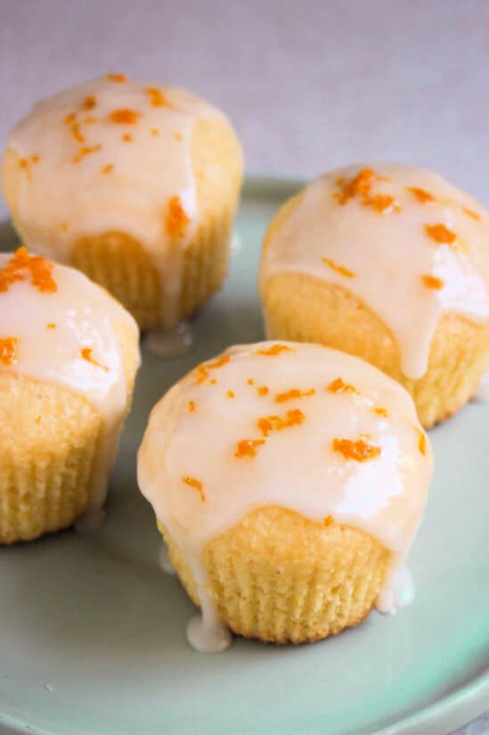 Orange coconut muffins with icing on an aqua-green plate.