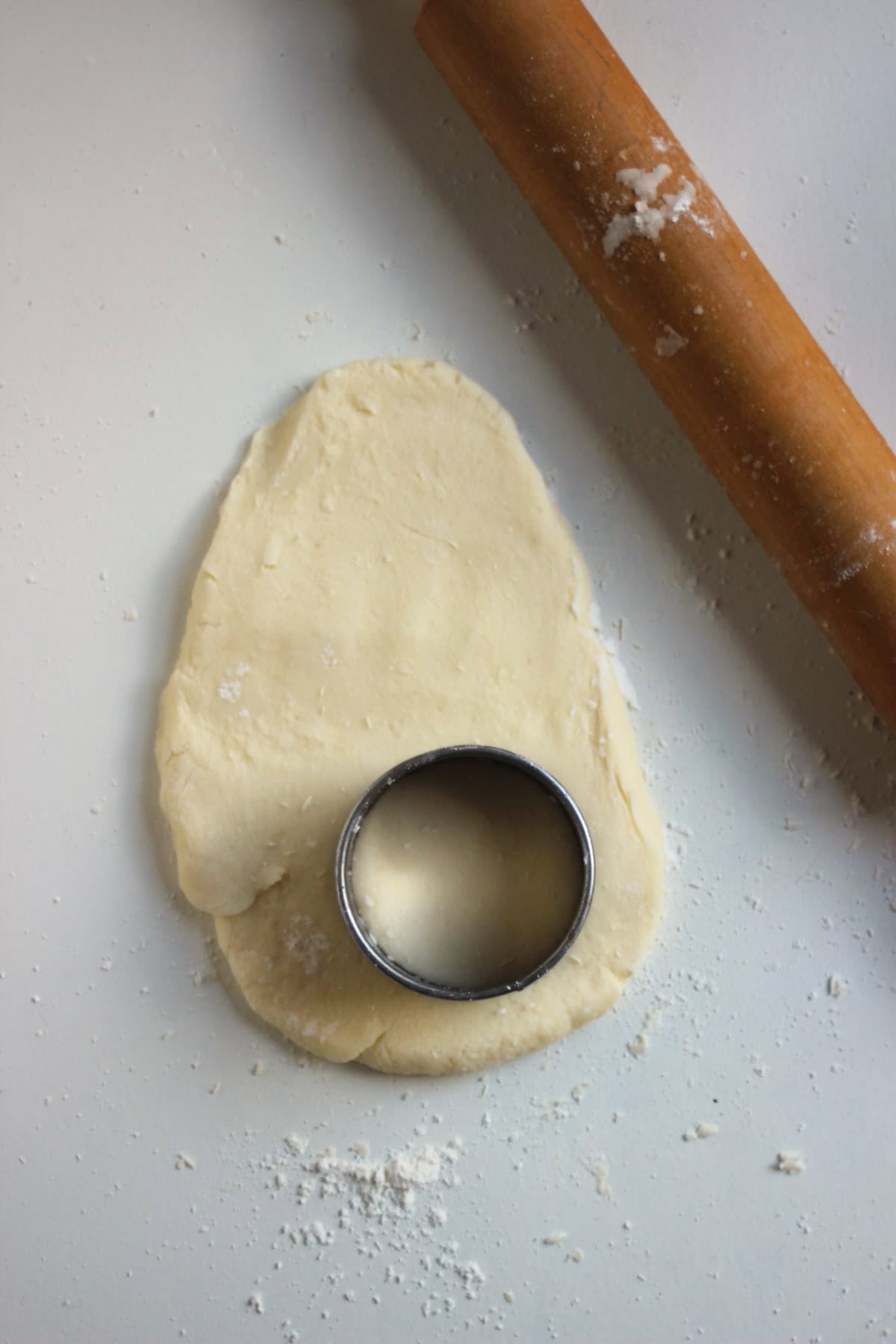 The stretched shortcake dough . A round biscuit cutter on on the dough and rolling pin on the side.