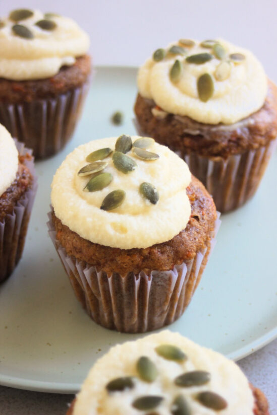 Carrot cake cupcakes with cream cheese frosting and pumpkin seeds on an aqua-green plate.