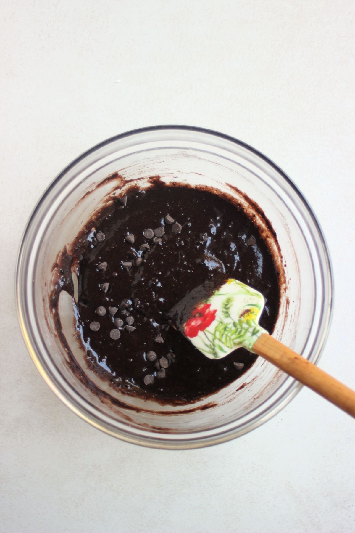 Glass bowl with a brown mixture and a rubber spatula.