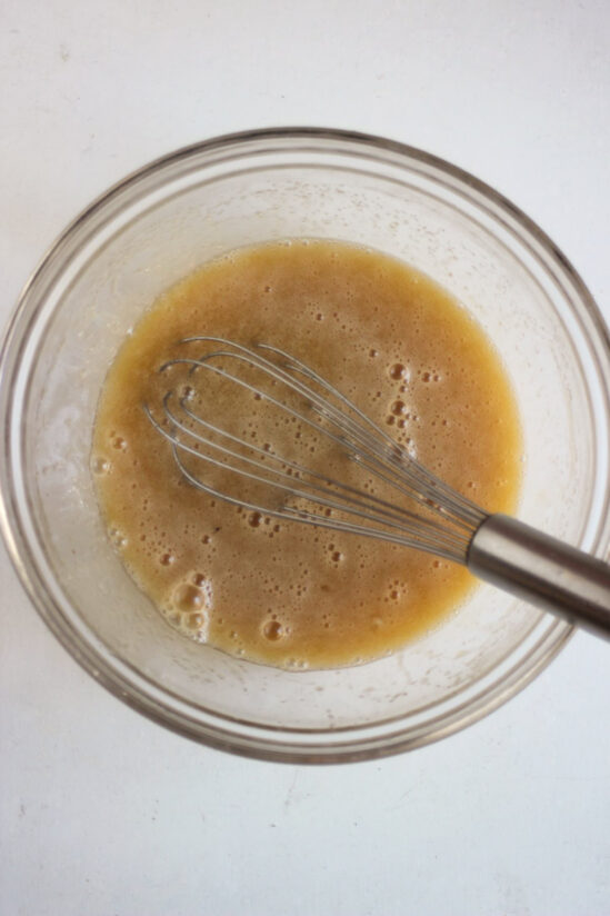 Glass bowl with a brown liquid and a hand whisk.