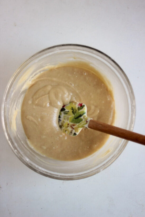 Glass bowl with a smooth, light brown mixture and a rubber spatula.