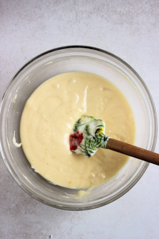 Glass bowl with a smooth, cream colour mixture and a rubber spatula.