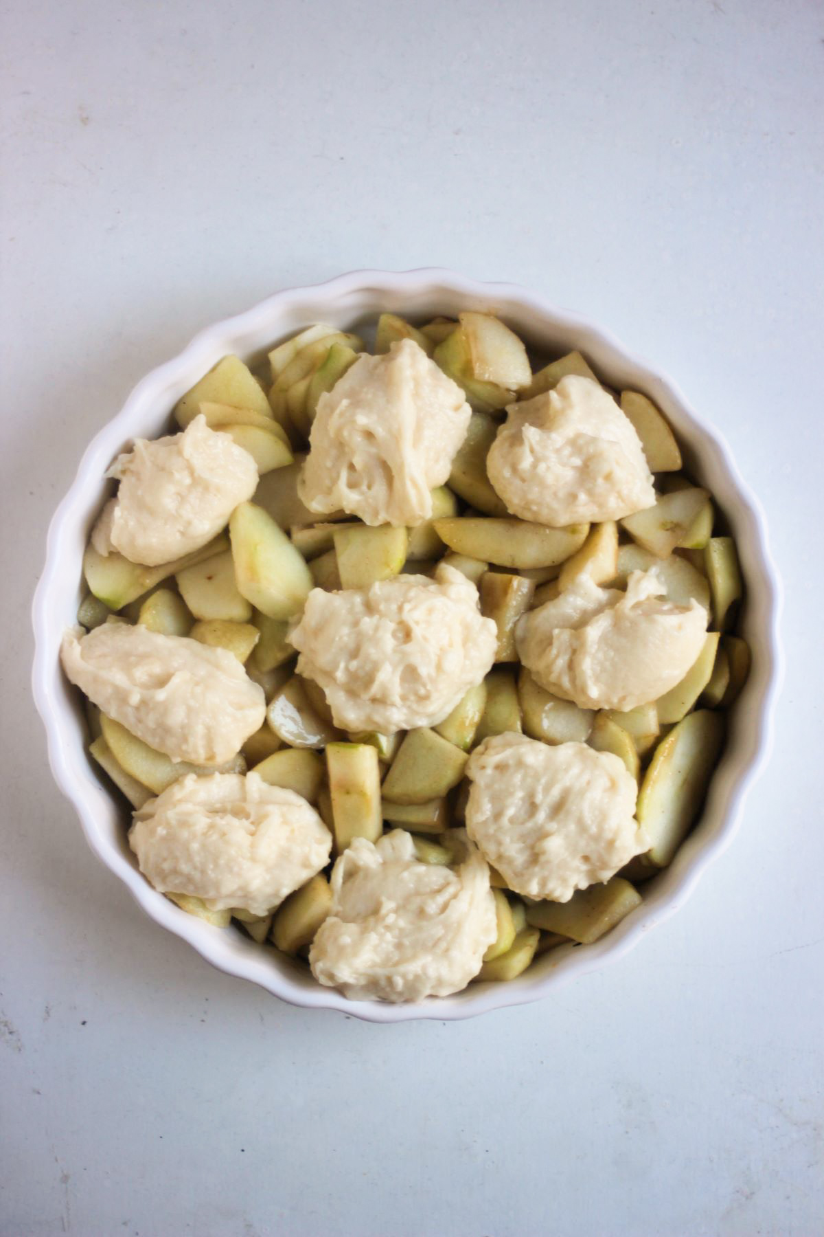 Round baking pan with sliced apples and scoops of dough seen from above.