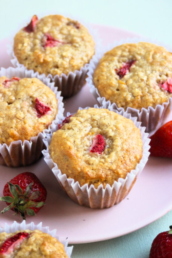 Strawberry oatmeal muffins with liners on a pink plate. Fresh strawberries on the sides.