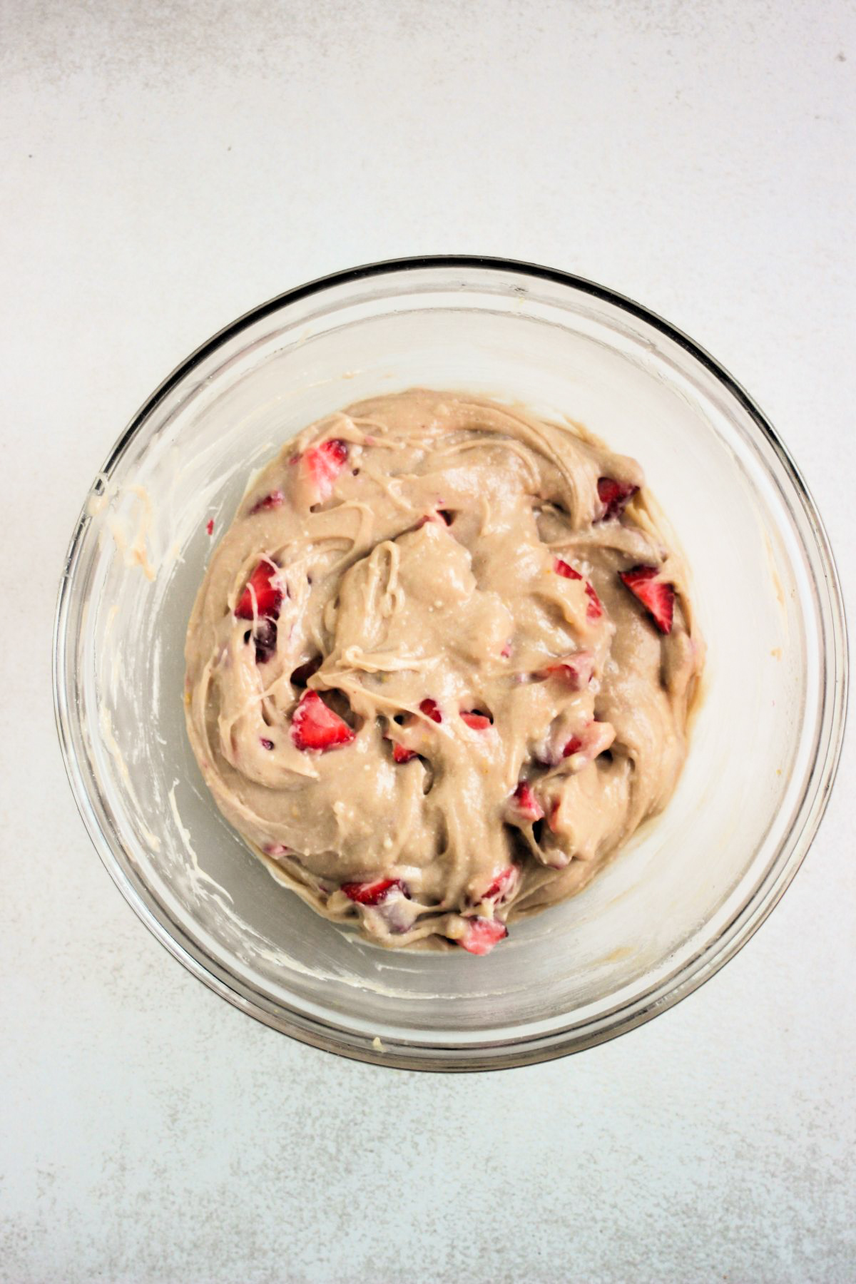 Top view of a glass bowl with a light brown mixture that includes sliced strawberries.
