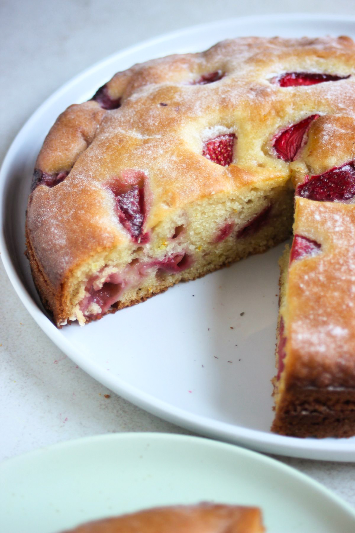 Partial view of strawberry cake without a portion on a white plate.