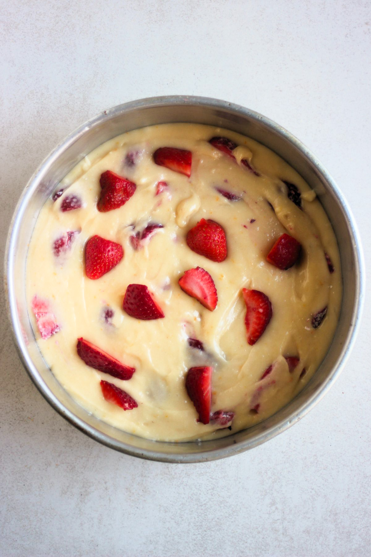 Top view of a round baking pan with a batter that includes fresh sliced strawberries.