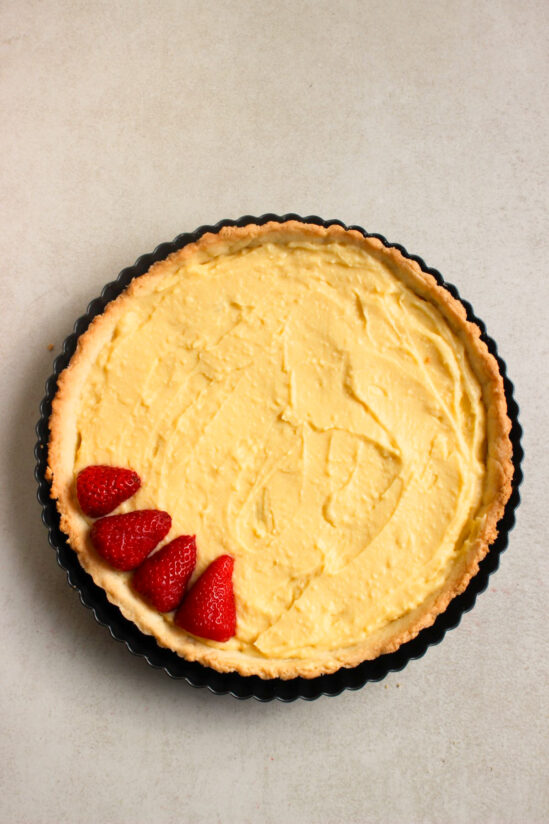 Top view of a strawberry tart crust in a round tart pan with vanilla pastry cream and four strawberry slices.