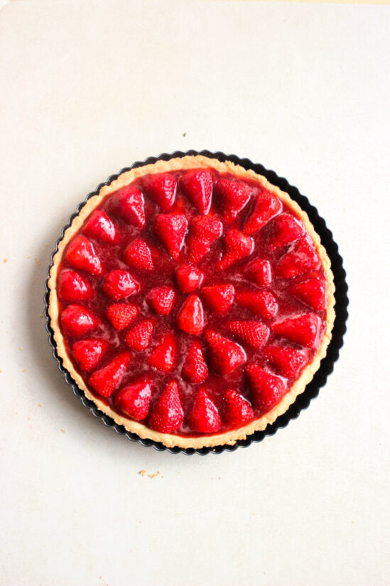 Top view of strawberry jelly tart on a round tart pan on a white surface.