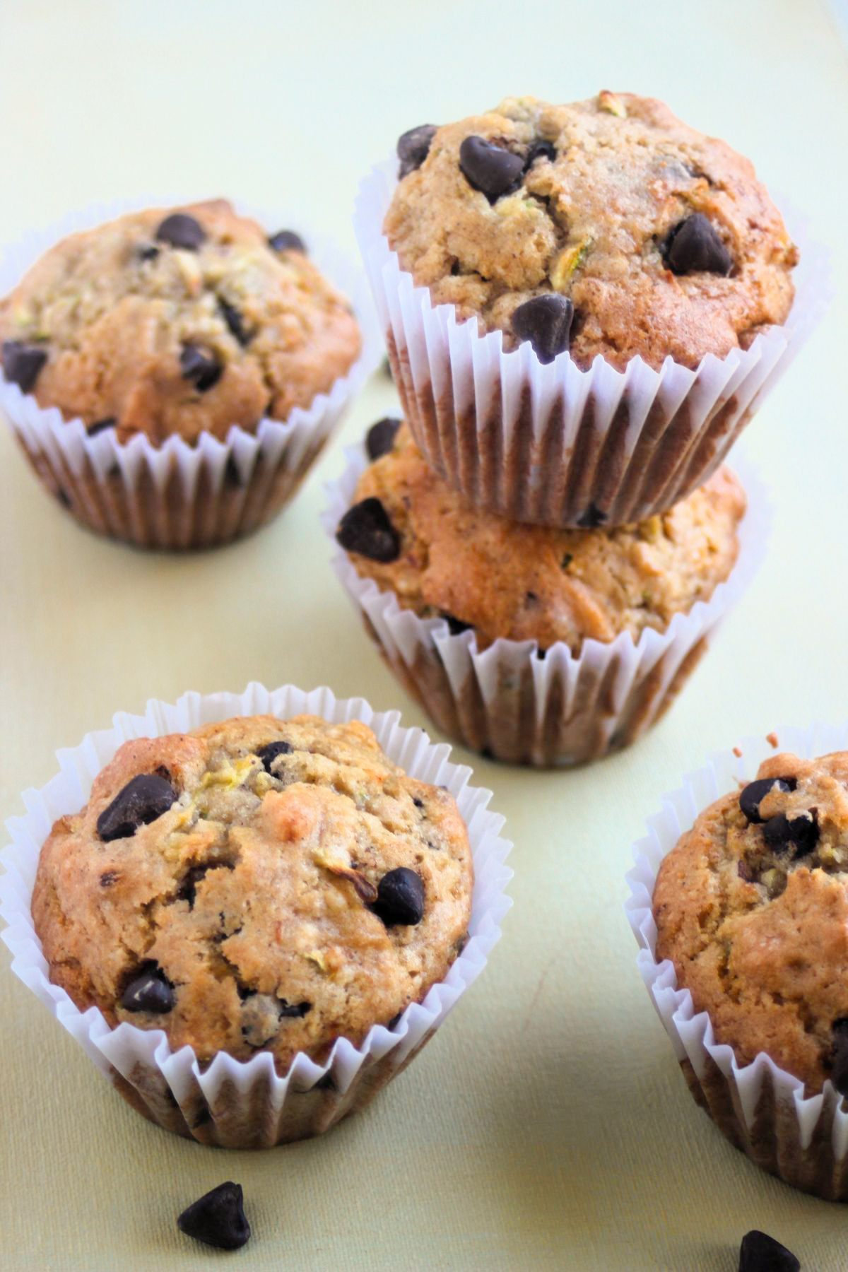 Zucchini chocolate chip muffins with liners on a light cream color surface.