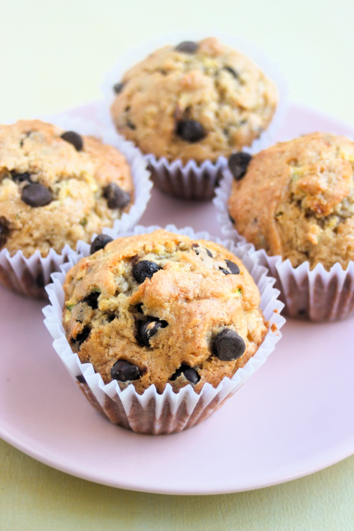 Zucchini chocolate chip muffins with liners on a pink plate.