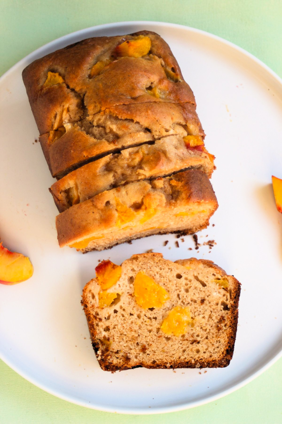 Top view of peach loaf cake and slices of it, on a white plate. Fresh peach slices on the sides.