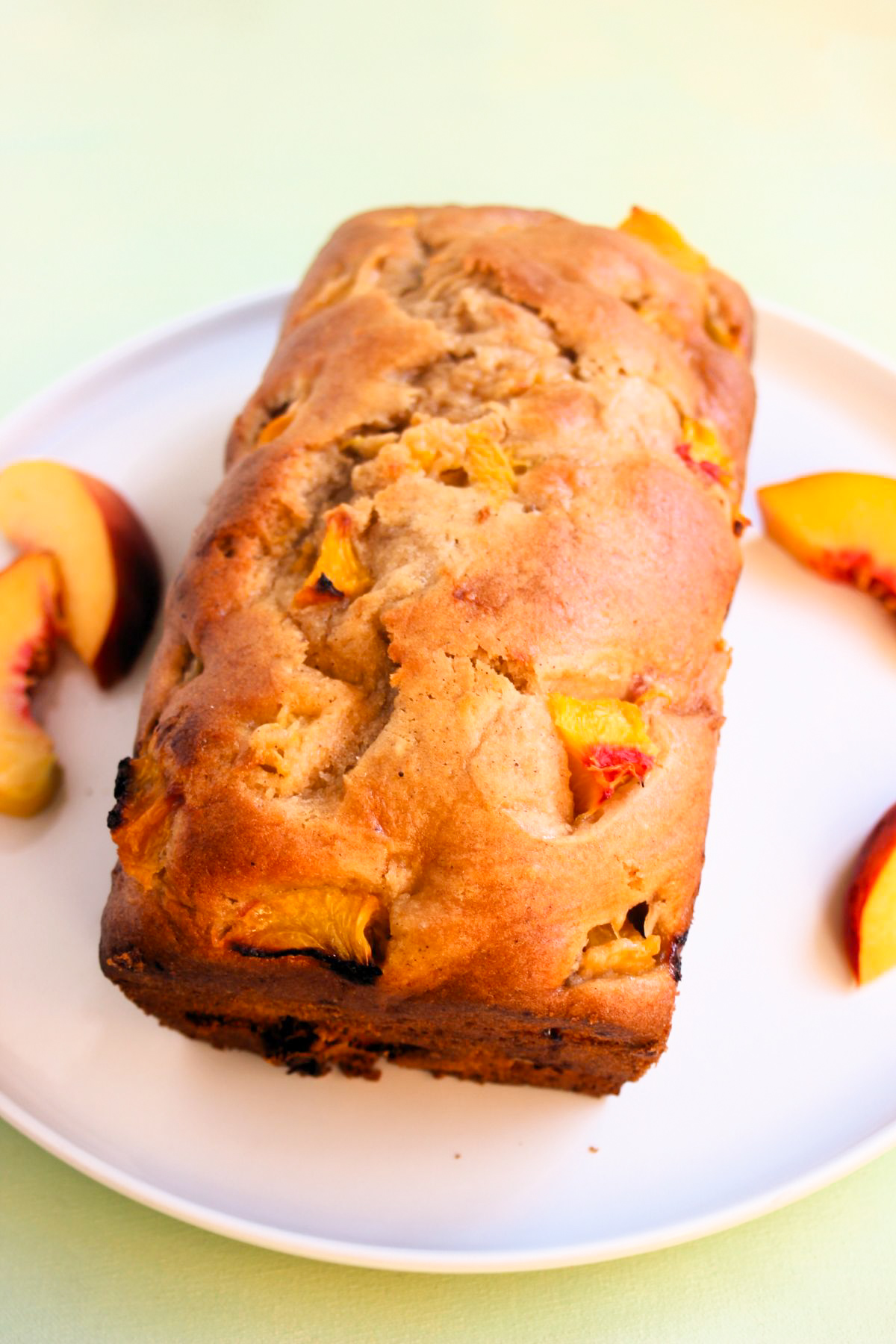 Peach loaf cake on a white plate. Fresh peach slices on the sides.
