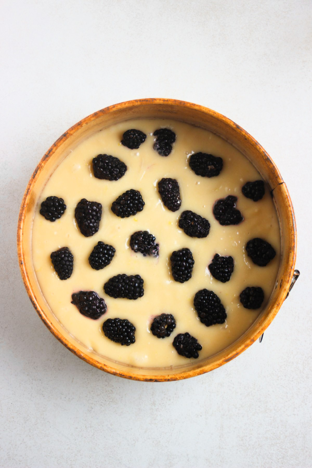 Top view of a round cake pan with batter and fresh blackberries on top.