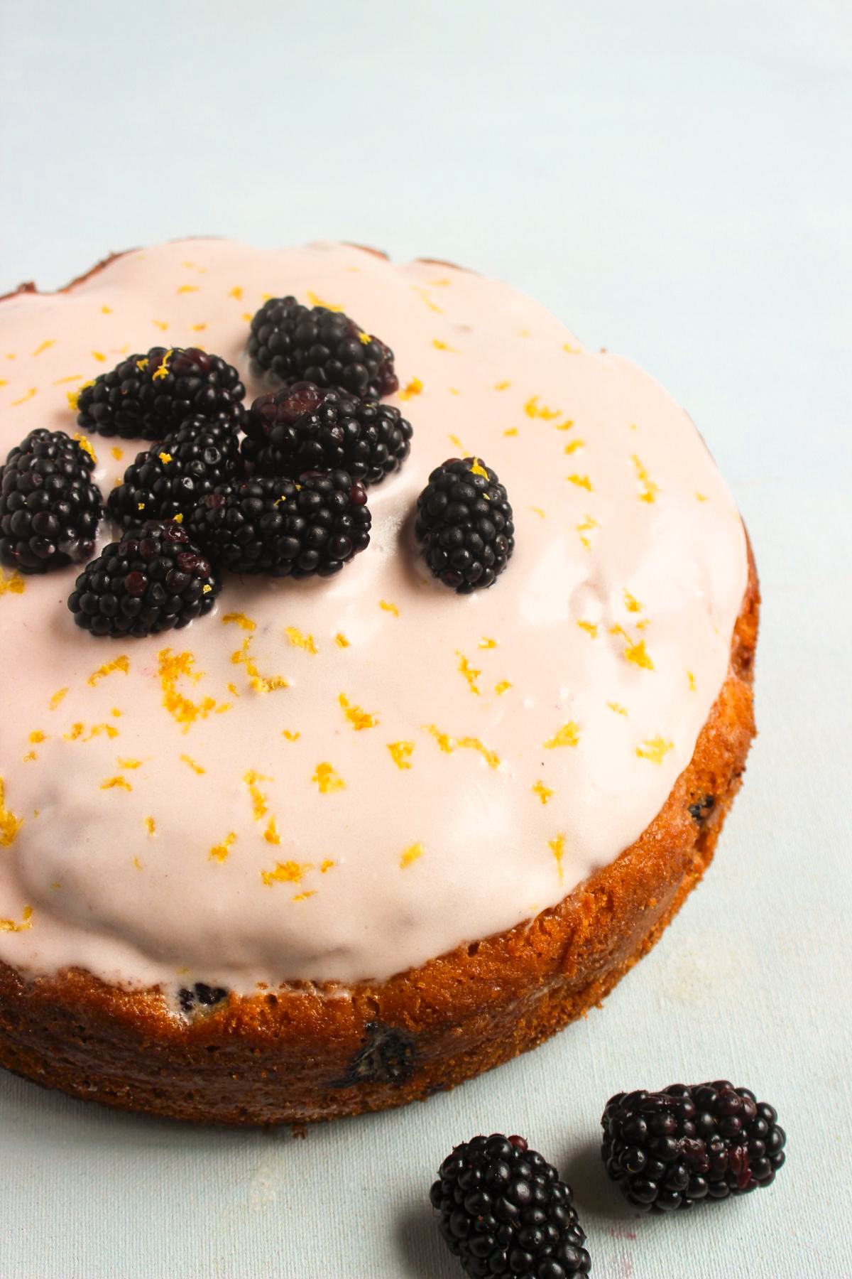 Blackberry cake with frosting and fresh blackberries on a light-blue surface.