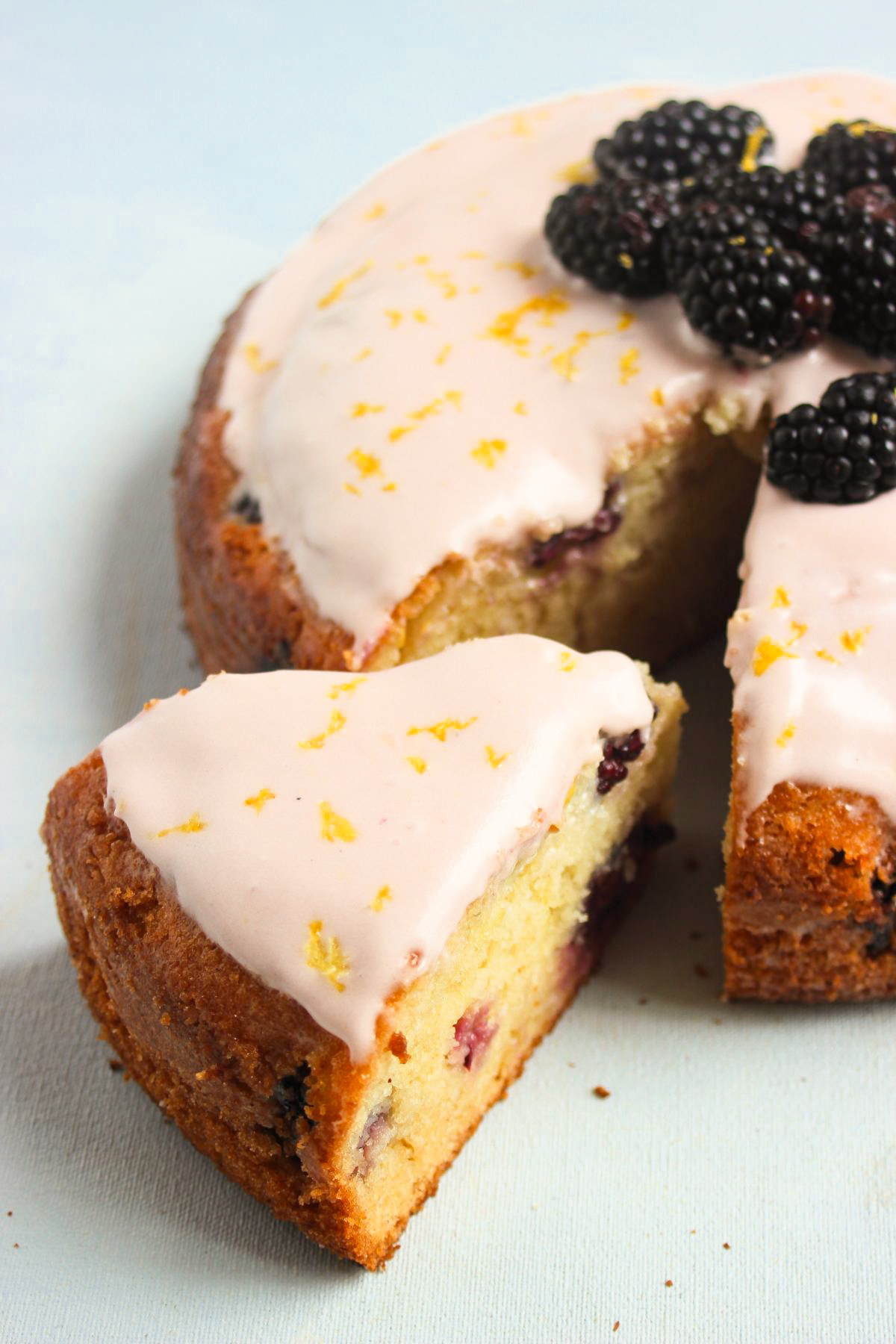 A portion on blackberry cakePortion of blackberry cake with frosting, and the whole cake next to it on a light-blue surface.