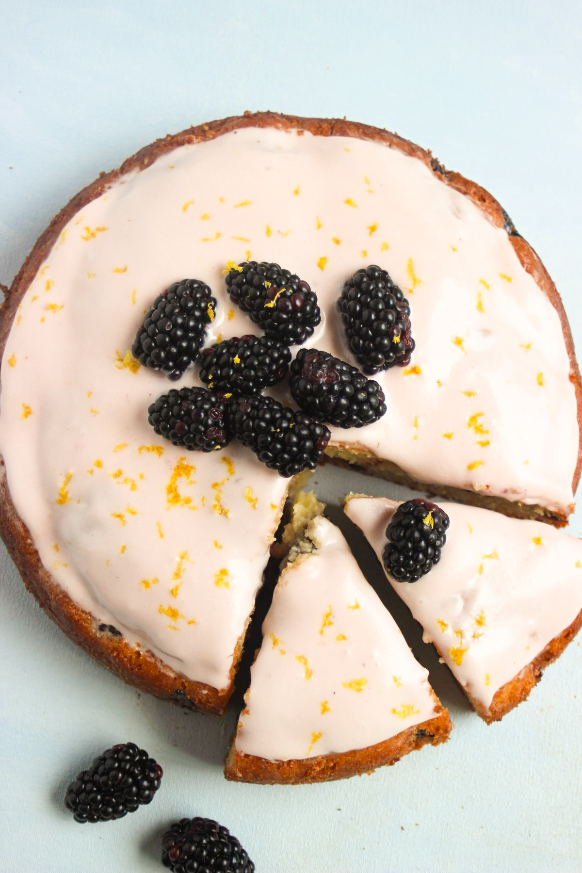 Top view of blackberry cake with frosting and fresh blackberries. Two portions are cut.