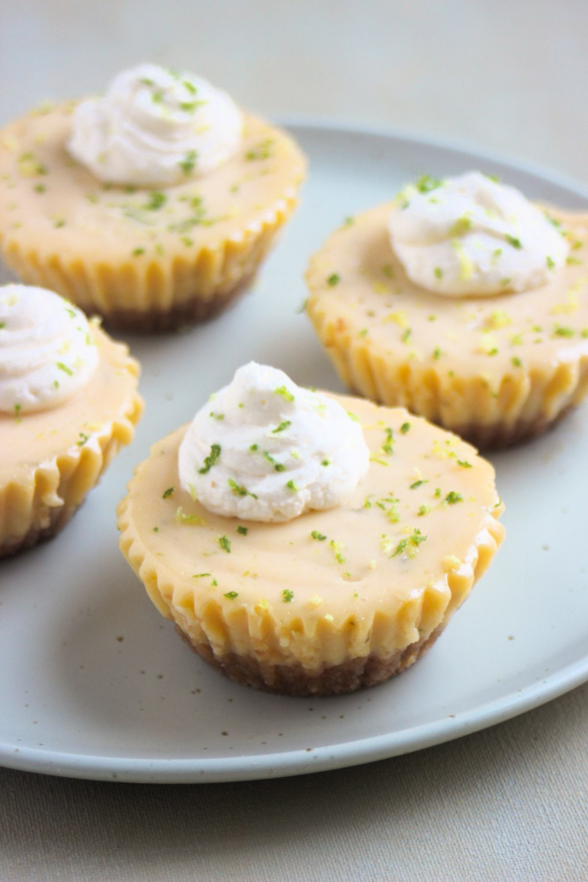 Mini key lime pie with whipped cream on an aqua-green plate. More mini cakes behind.