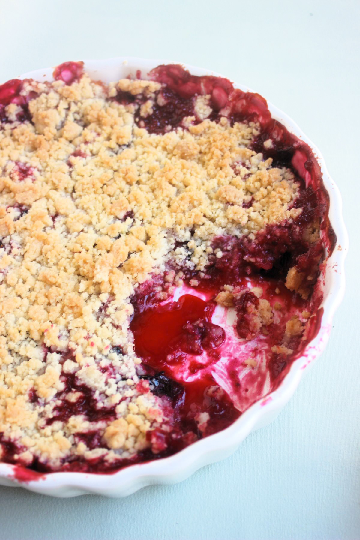 Partial view of a round baking dish with plum crumble without a portion.