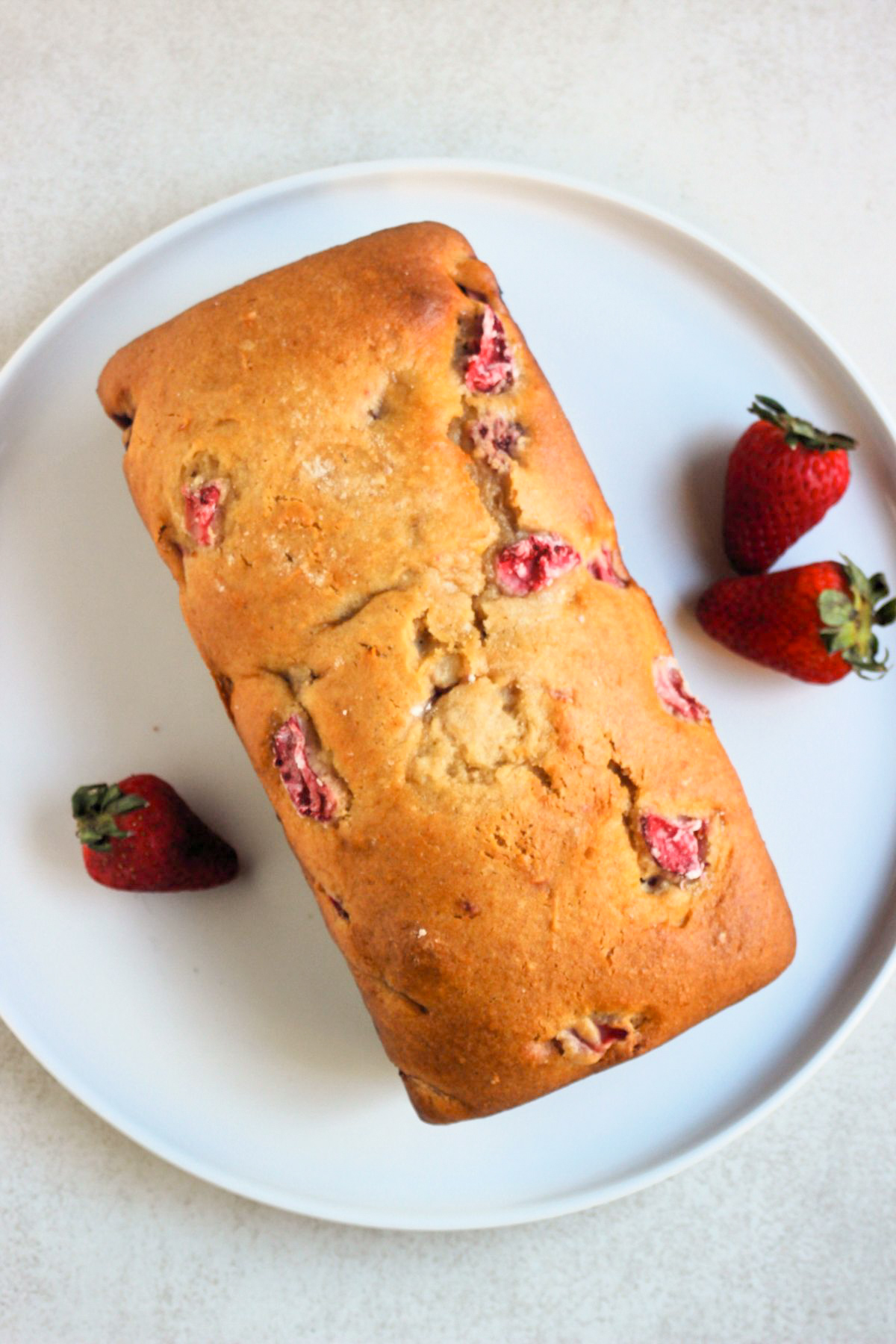 Top view of strawberry bread on a white plate. Fresh strawberries on the side.