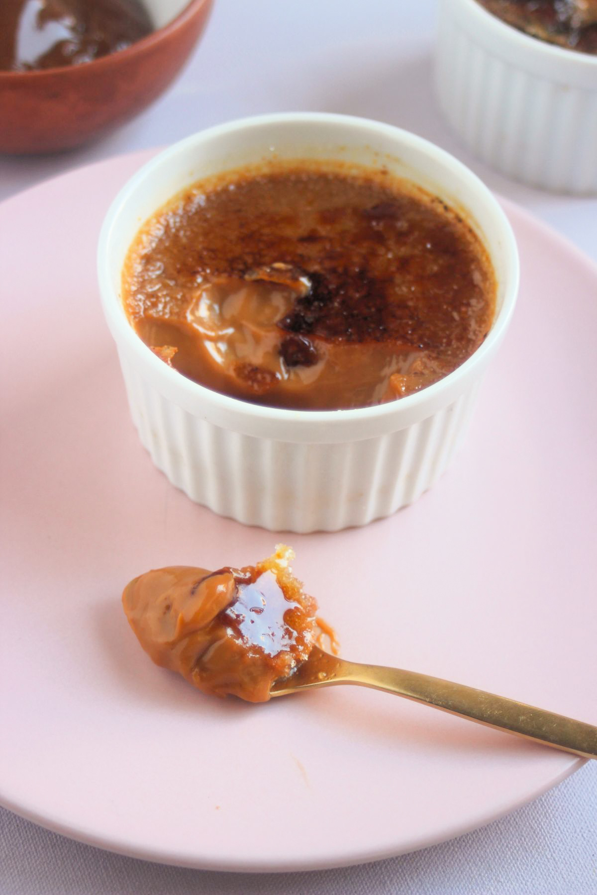 A partially eaten crème brûlée on a pink plate and a spoon with crème brûlée.
