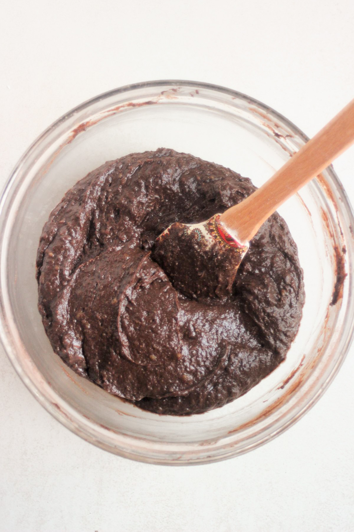 Glass bowl with a brown mixture and a rubber spatula.