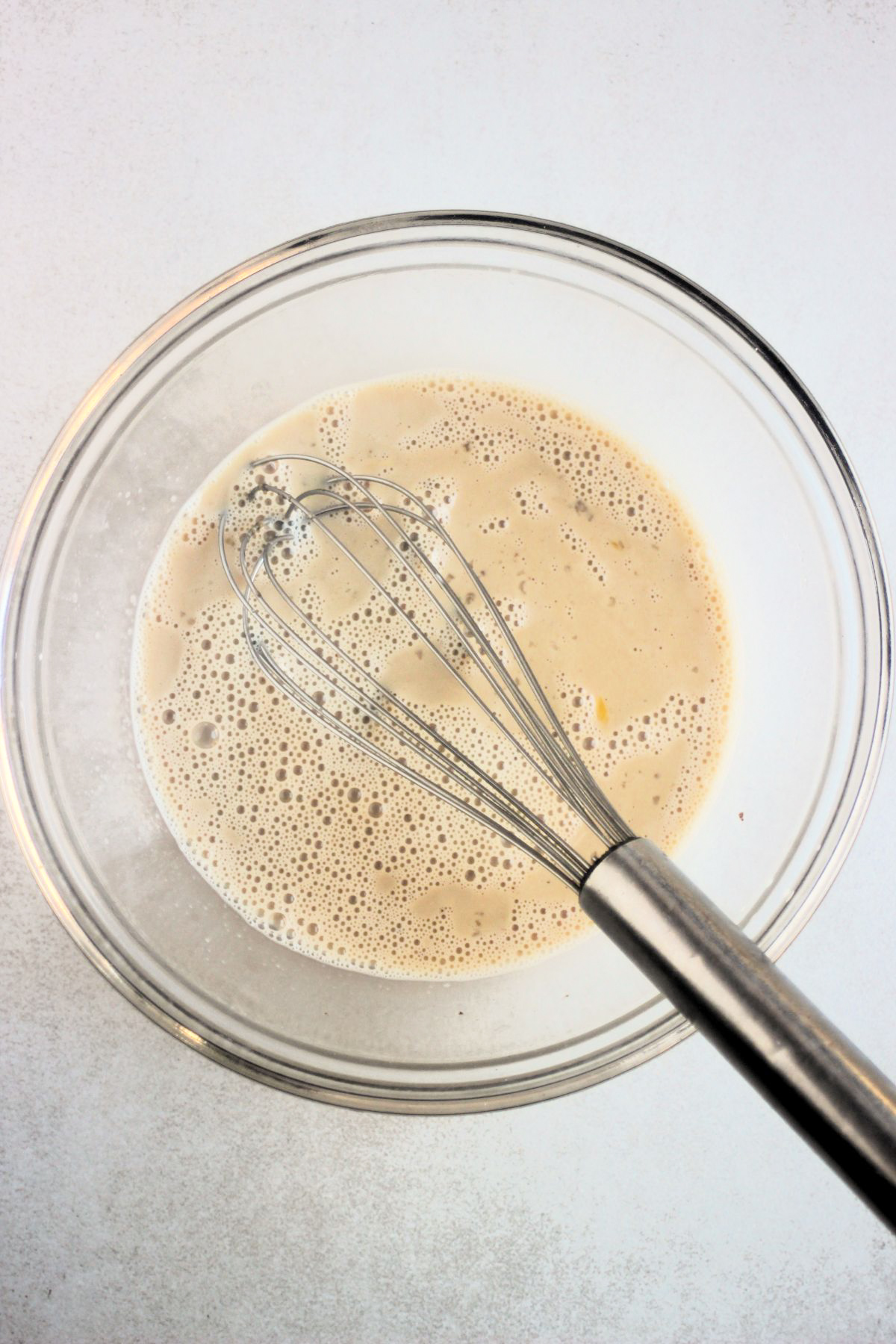 A glass bowl with a liquid and a hand whisk.