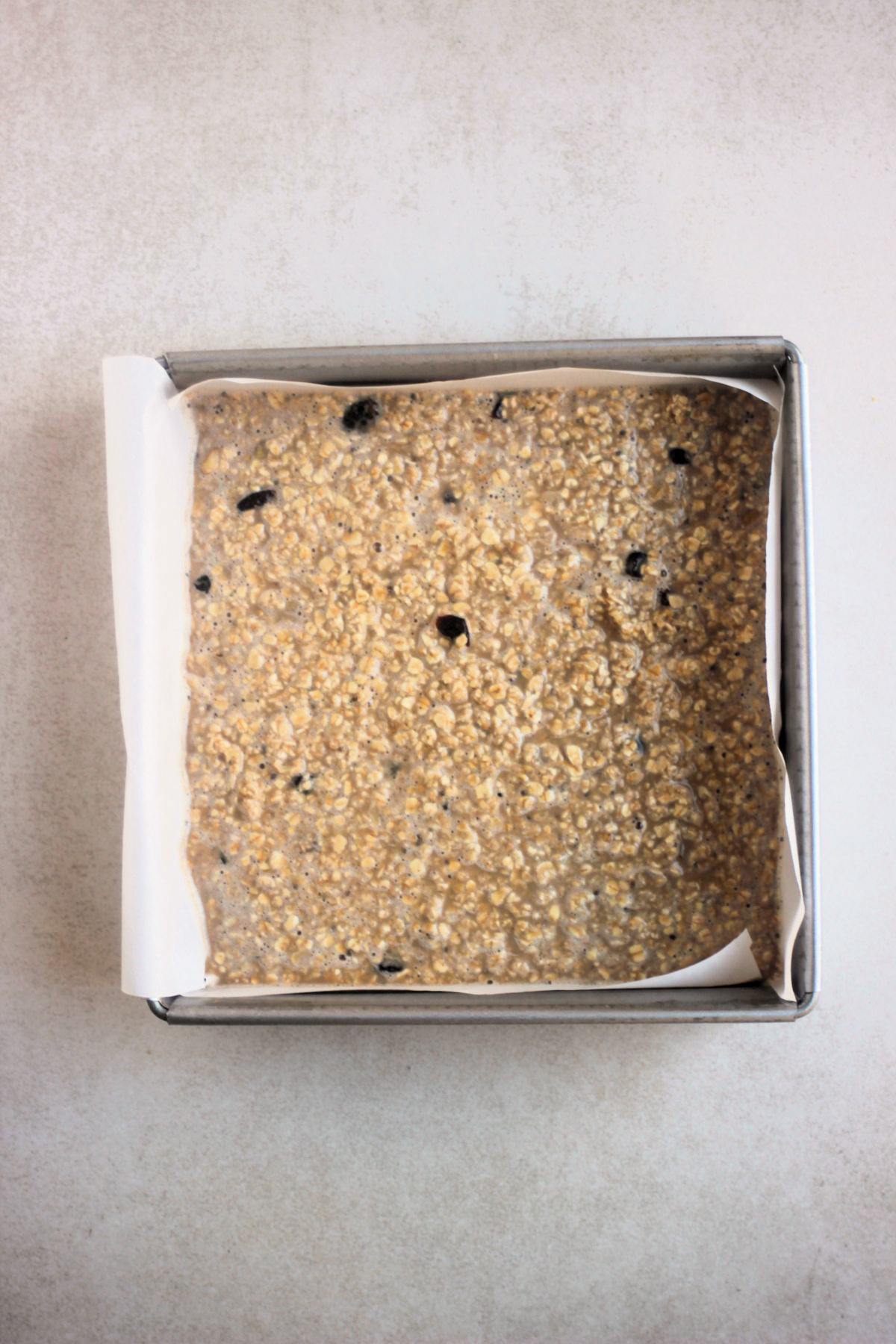 Top view of a square baking pan with parchment paper, with a mixture that includes oats.