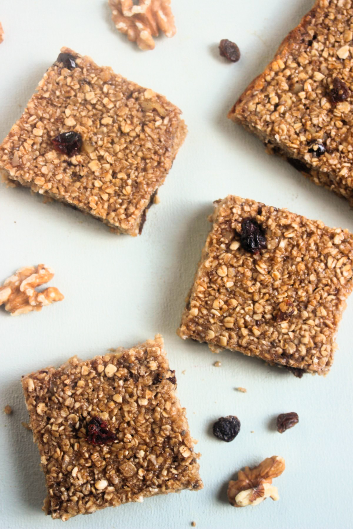 Top view of baked oatmeal bars on a white surface. Raisins and walnuts are scattered around.