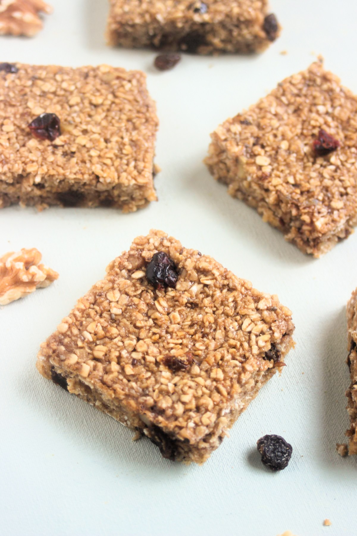 Baked oatmeal bars on a white surface. Raisins and walnuts are scattered around.